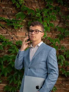 Dorian Drgonec im Anzug telefoniert und hält ein MacBook, wie ein ganz normaler seriöser CEO